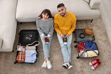Couple with passports and tickets near suitcases on floor indoors, top view