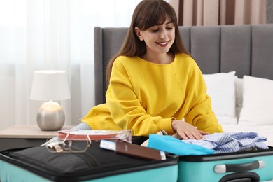 Woman packing suitcase for trip on bed indoors