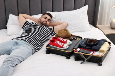 Man near suitcase with clothes on bed indoors