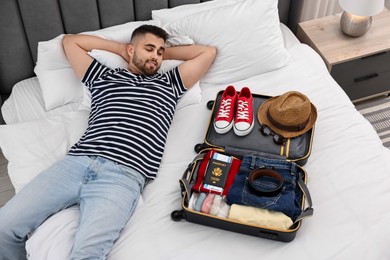 Photo of Man near suitcase with clothes on bed indoors