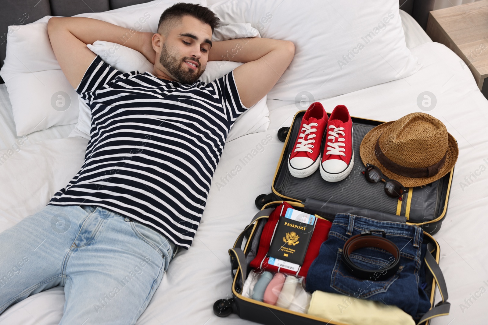 Photo of Man near suitcase with clothes on bed indoors