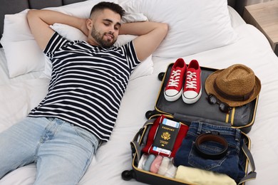 Photo of Man near suitcase with clothes on bed indoors