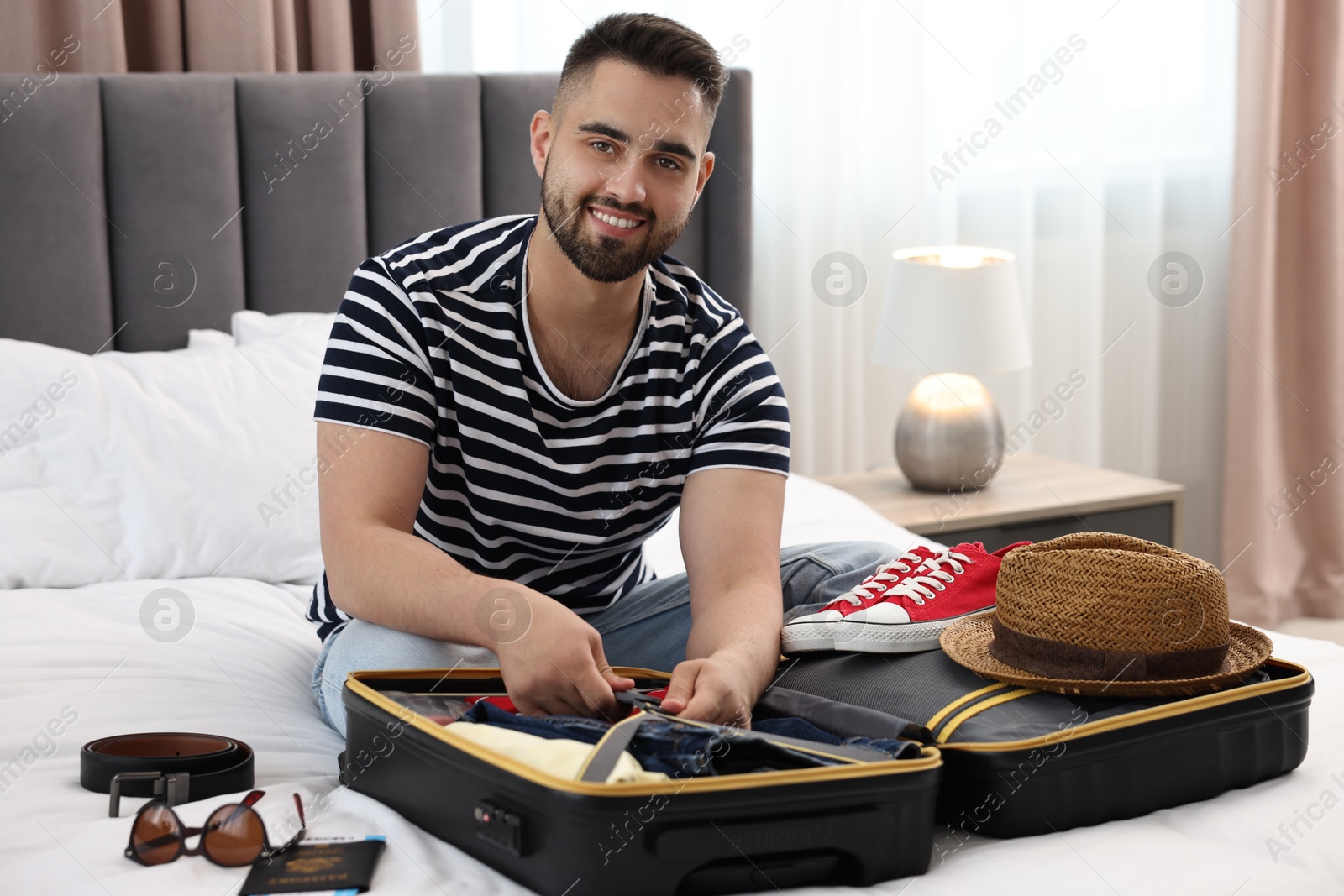 Photo of Man packing suitcase for trip on bed indoors