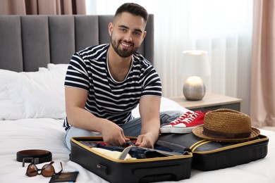 Man packing suitcase for trip on bed indoors
