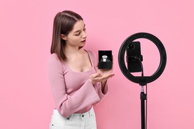 Photo of Fashion blogger reviewing watch and recording video with smartphone and ring lamp on pink background