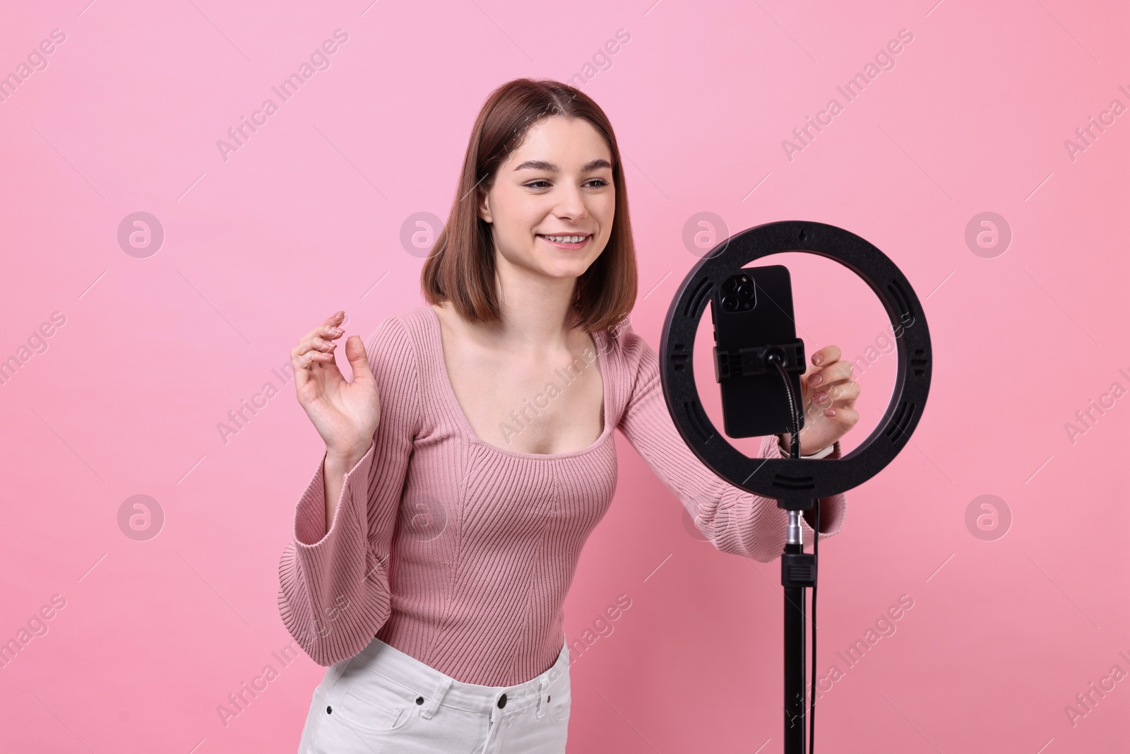 Photo of Blogger recording video with smartphone and ring lamp on pink background