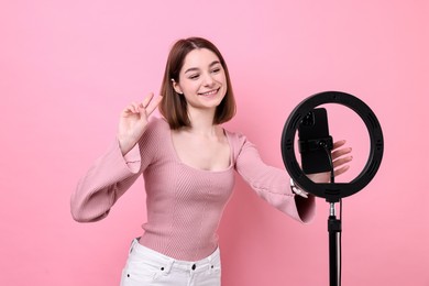 Photo of Blogger recording video with smartphone and ring lamp on pink background