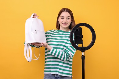 Fashion blogger reviewing backpack and recording video with smartphone and ring lamp on orange background