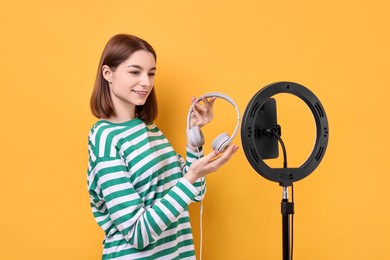 Technology blogger reviewing headphones and recording video with smartphone and ring lamp on orange background