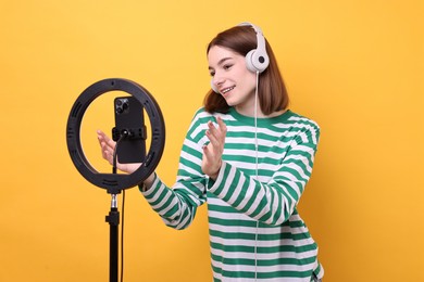 Photo of Technology blogger reviewing headphones and recording video with smartphone and ring lamp on orange background