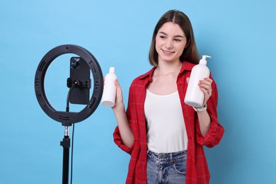 Photo of Beauty blogger reviewing cosmetic products and recording video with smartphone and ring lamp on light blue background