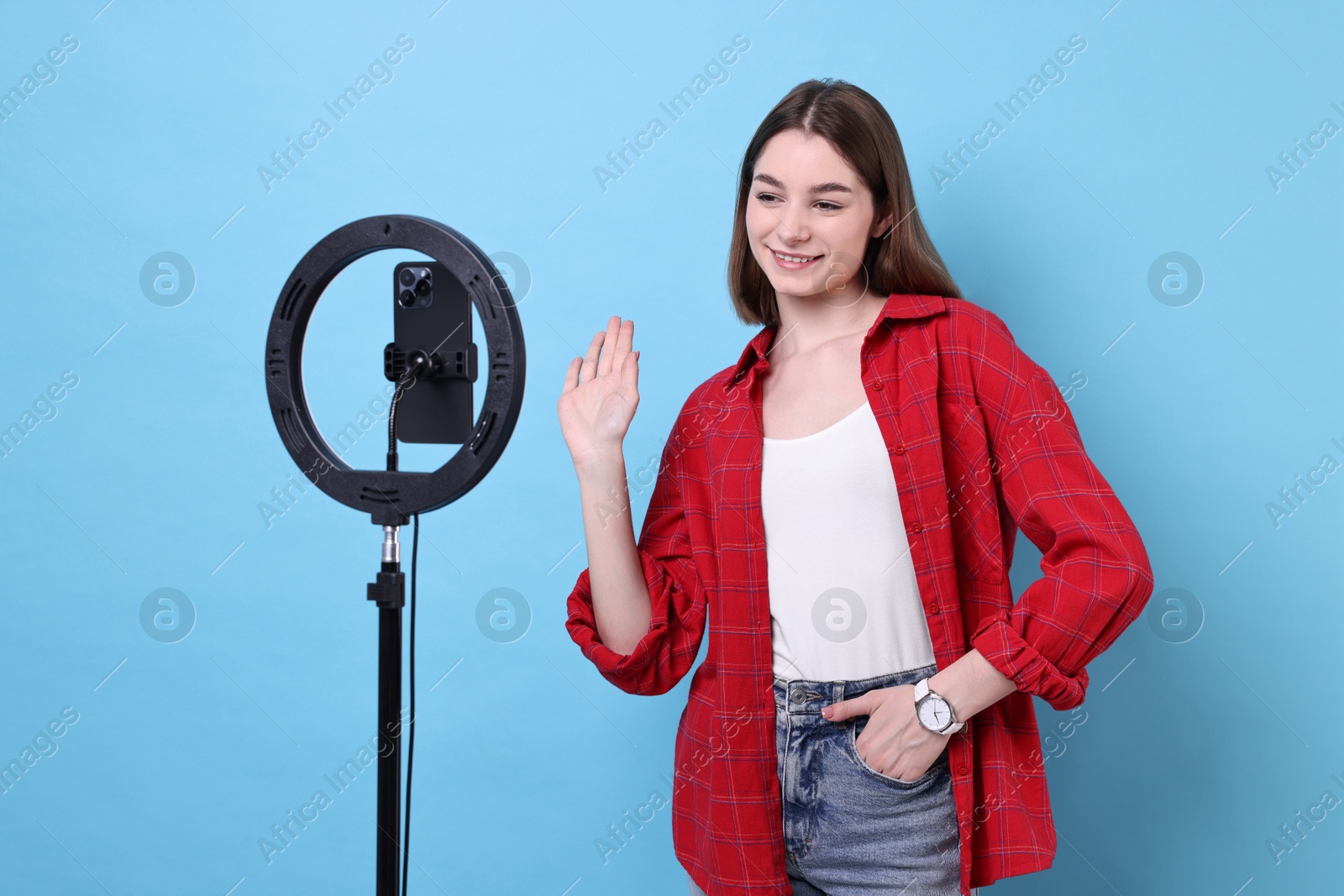 Photo of Blogger recording video with smartphone and ring lamp on light blue background