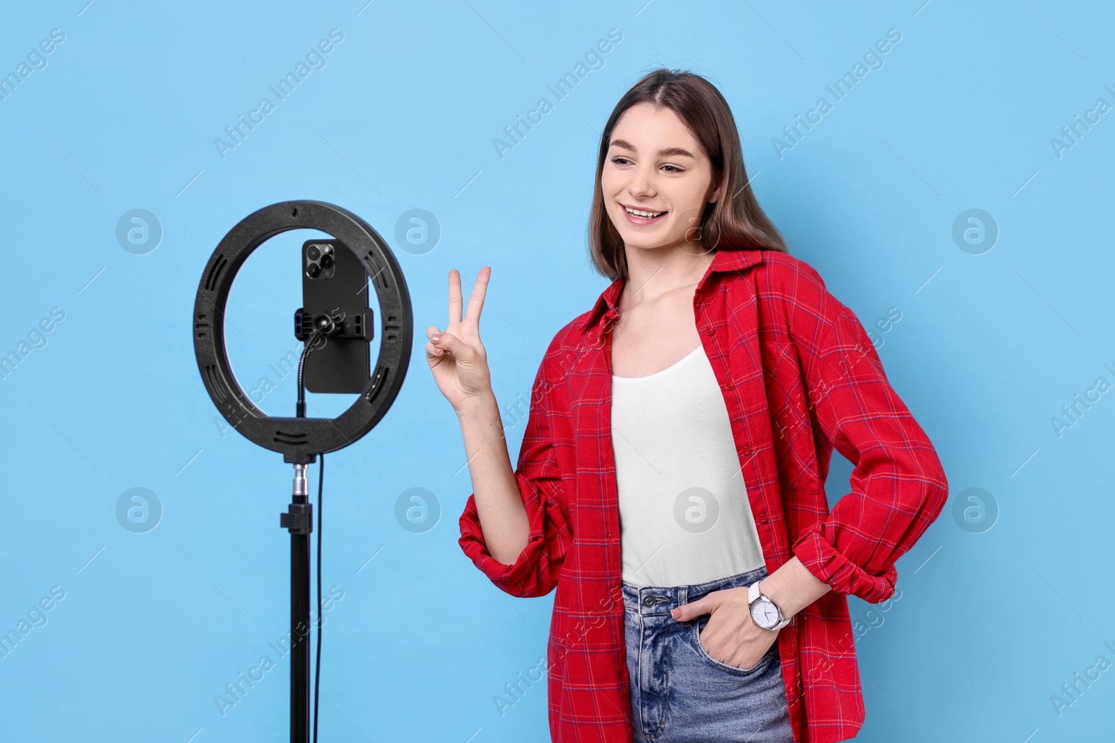 Photo of Blogger recording video with smartphone and ring lamp on light blue background