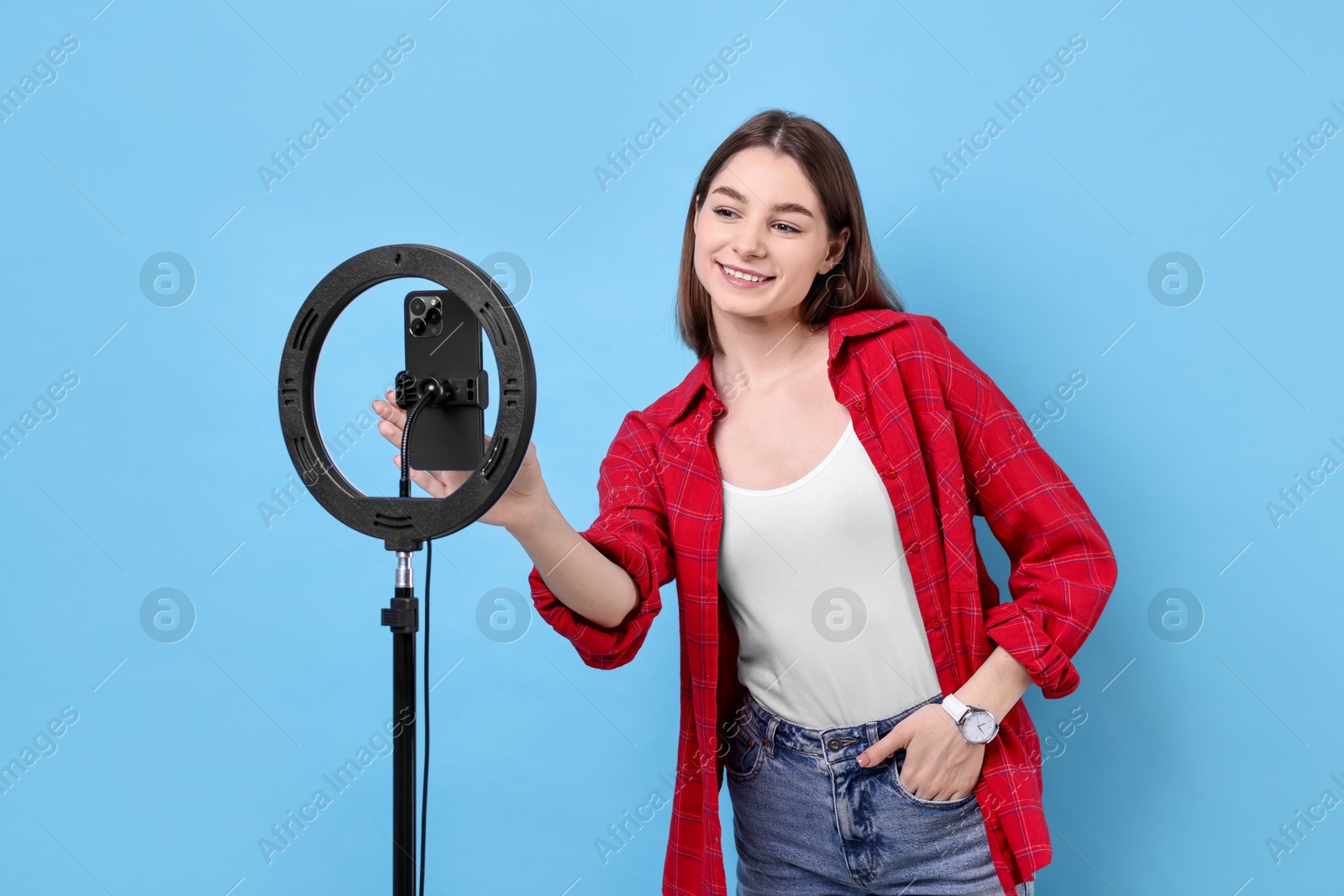 Photo of Blogger recording video with smartphone and ring lamp on light blue background