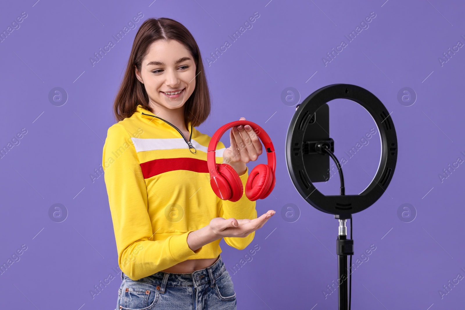 Photo of Technology blogger reviewing headphones and recording video with smartphone and ring lamp on purple background