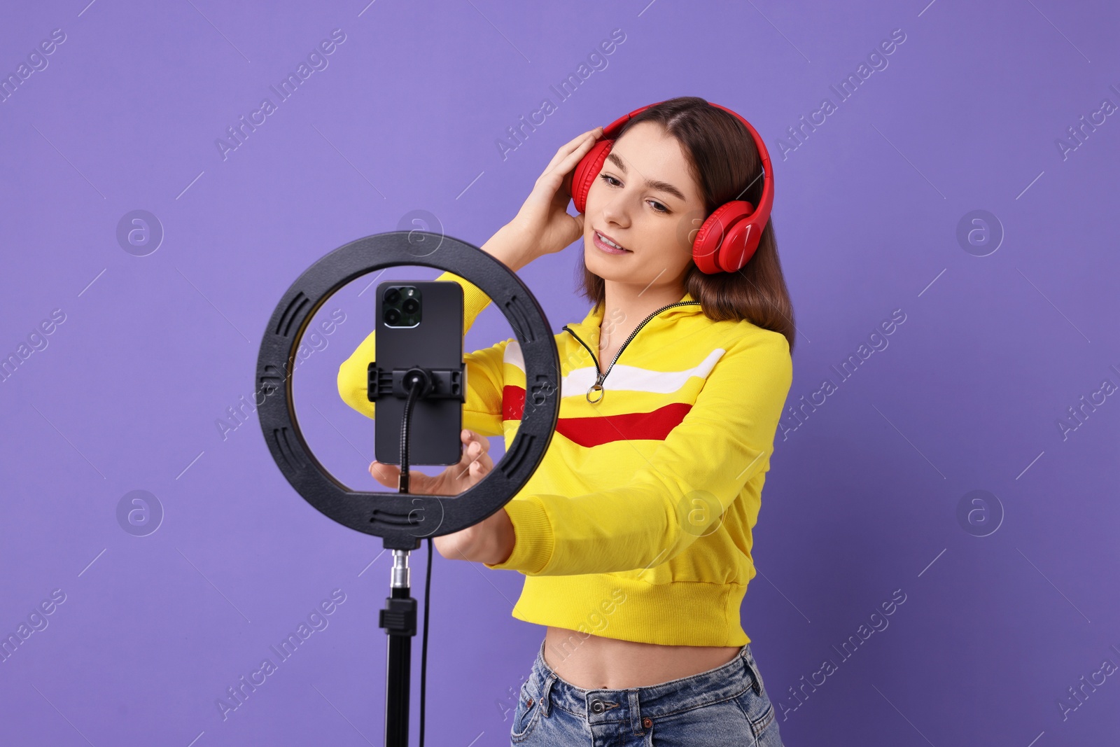 Photo of Technology blogger reviewing headphones and recording video with smartphone and ring lamp on purple background