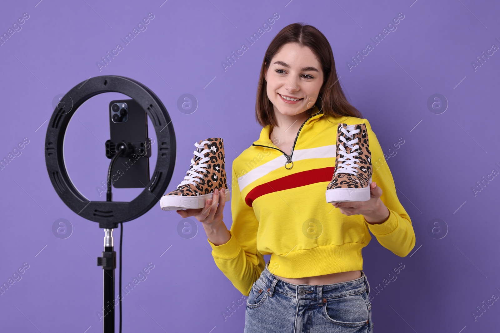 Photo of Fashion blogger reviewing sneakers and recording video with smartphone and ring lamp on purple background