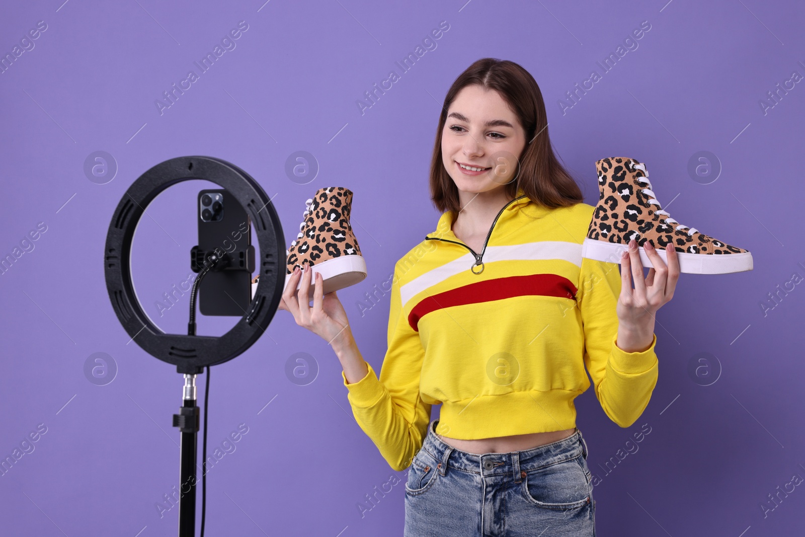 Photo of Fashion blogger reviewing sneakers and recording video with smartphone and ring lamp on purple background