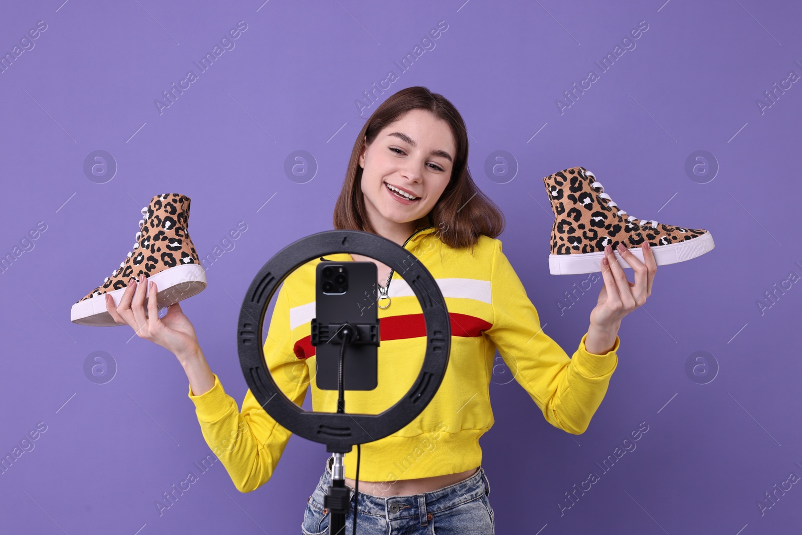 Photo of Fashion blogger reviewing sneakers and recording video with smartphone and ring lamp on purple background