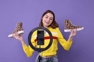 Fashion blogger reviewing sneakers and recording video with smartphone and ring lamp on purple background