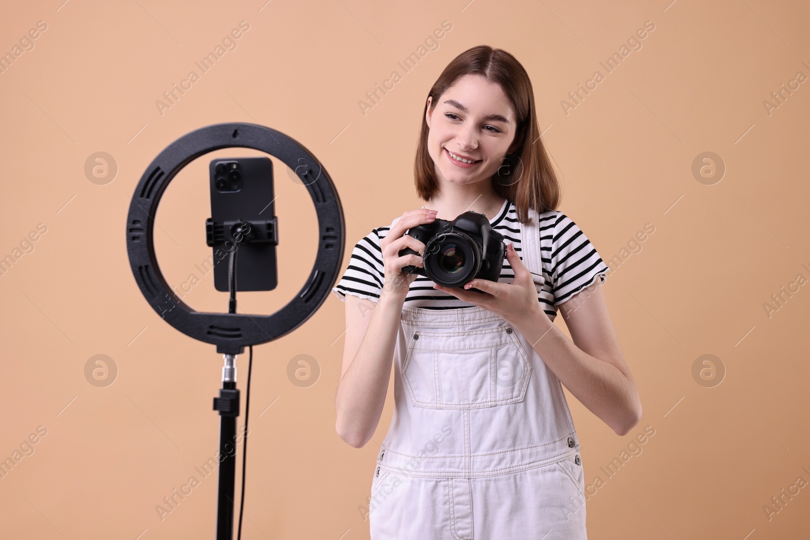 Photo of Technology blogger reviewing camera and recording video with smartphone and ring lamp on beige background