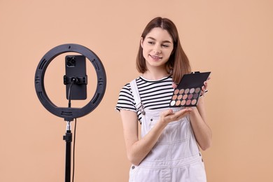 Photo of Beauty blogger reviewing eyeshadows and recording video with smartphone and ring lamp on beige background