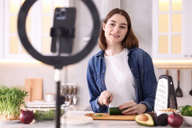 Food blogger cooking while recording video with smartphone and ring lamp in kitchen