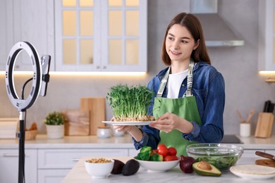 Food blogger cooking while recording video with smartphone and ring lamp in kitchen