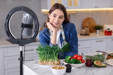 Food blogger cooking while recording video with smartphone and ring lamp in kitchen