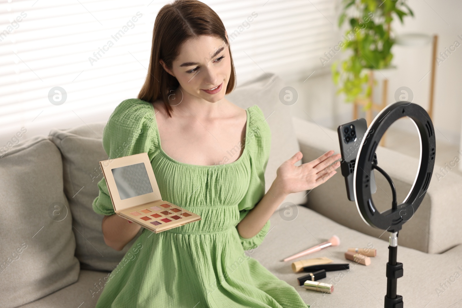 Photo of Beauty blogger reviewing eyeshadows and recording video with smartphone and ring lamp at home