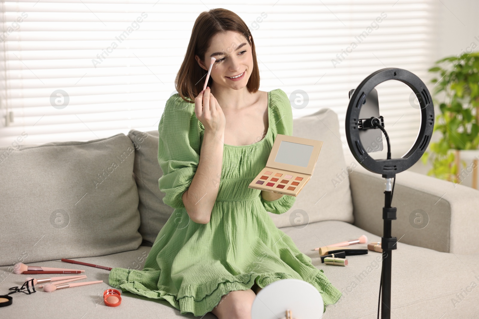 Photo of Beauty blogger reviewing eyeshadows and recording video with smartphone and ring lamp at home