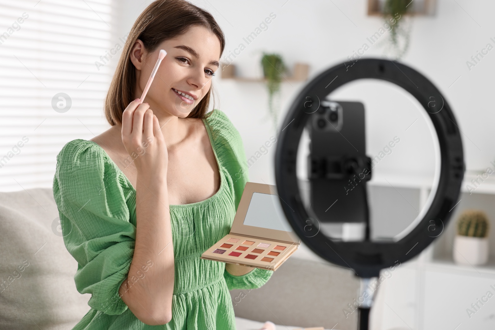 Photo of Beauty blogger reviewing eyeshadows and recording video with smartphone and ring lamp at home