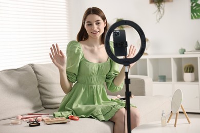 Photo of Beauty blogger reviewing decorative cosmetic products and recording video with smartphone and ring lamp at home