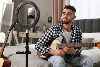 Photo of Music blogger recording guitar lesson with smartphone and ring lamp at home