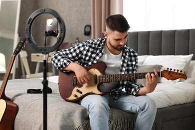 Photo of Music blogger recording guitar lesson with smartphone and ring lamp at home