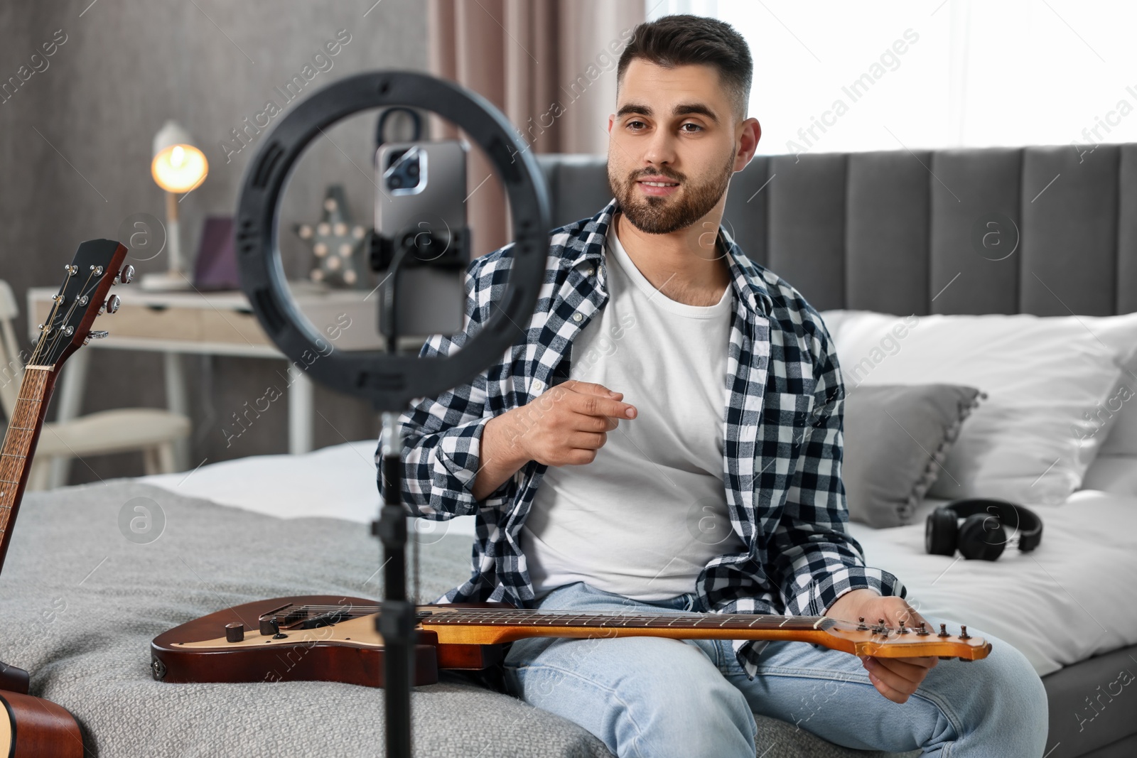 Photo of Music blogger recording guitar lesson with smartphone and ring lamp at home