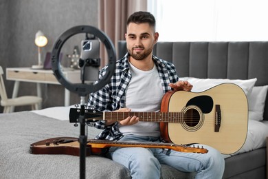 Photo of Music blogger recording guitar lesson with smartphone and ring lamp at home