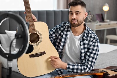 Photo of Music blogger recording guitar lesson with smartphone and ring lamp at home