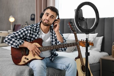 Photo of Music blogger recording guitar lesson with smartphone and ring lamp at home