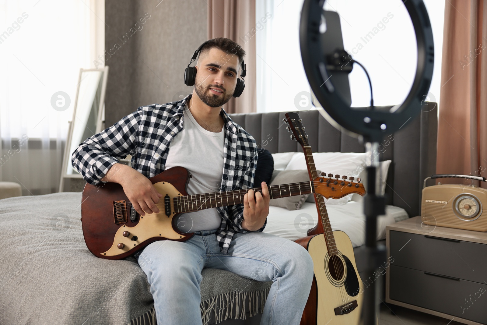 Photo of Music blogger recording guitar lesson with smartphone and ring lamp at home