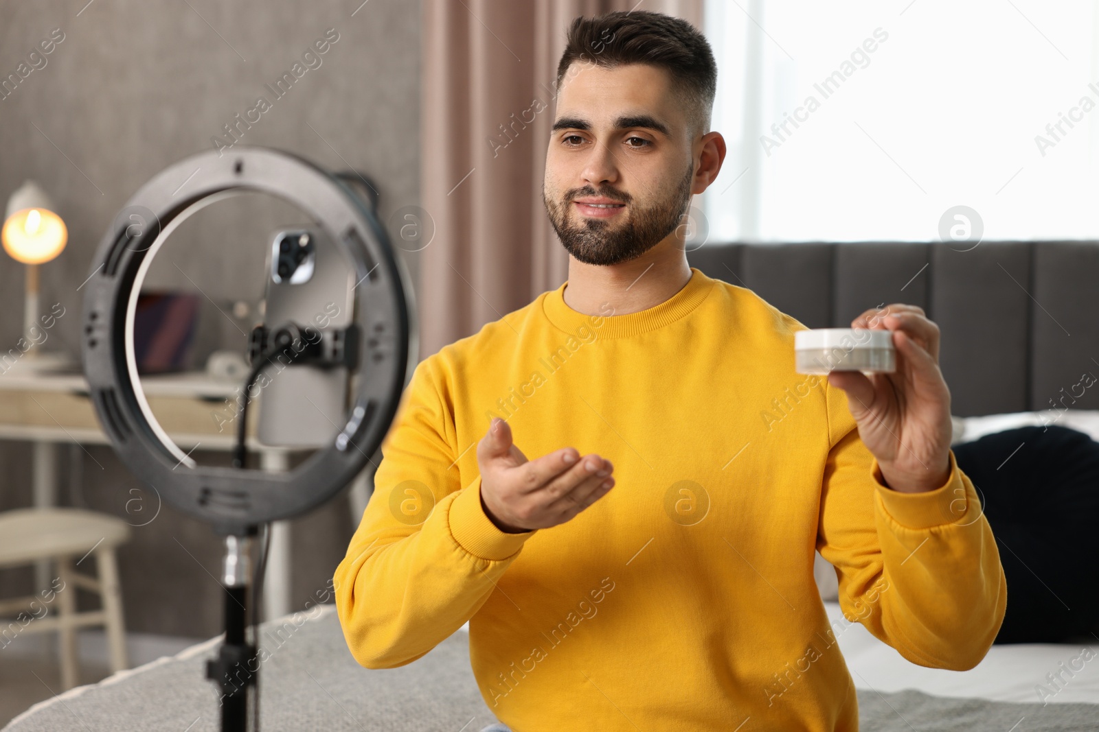 Photo of Beauty blogger reviewing cosmetic product and recording video with smartphone and ring lamp at home