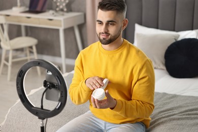 Beauty blogger reviewing cosmetic product and recording video with smartphone and ring lamp at home