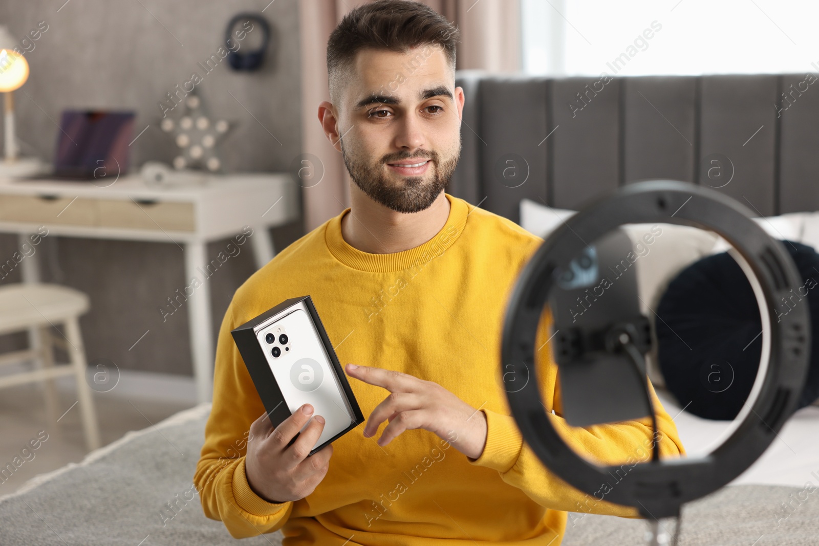 Photo of Technology blogger reviewing phone and recording video with smartphone and ring lamp at home