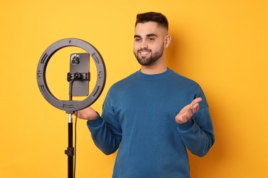 Photo of Blogger recording video with smartphone and ring lamp on orange background