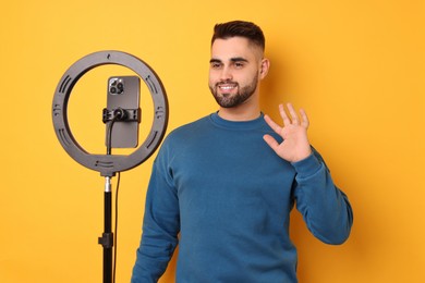 Photo of Blogger recording video with smartphone and ring lamp on orange background