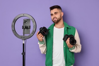 Technology blogger reviewing cameras and recording video with smartphone and ring lamp on purple background