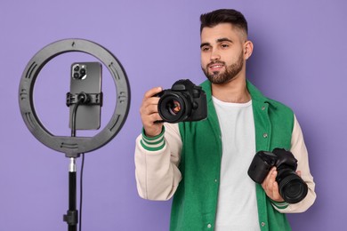 Photo of Technology blogger reviewing cameras and recording video with smartphone and ring lamp on purple background