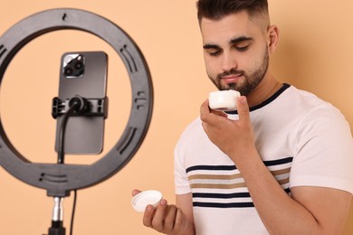 Photo of Beauty blogger reviewing cosmetic product and recording video with smartphone and ring lamp on beige background