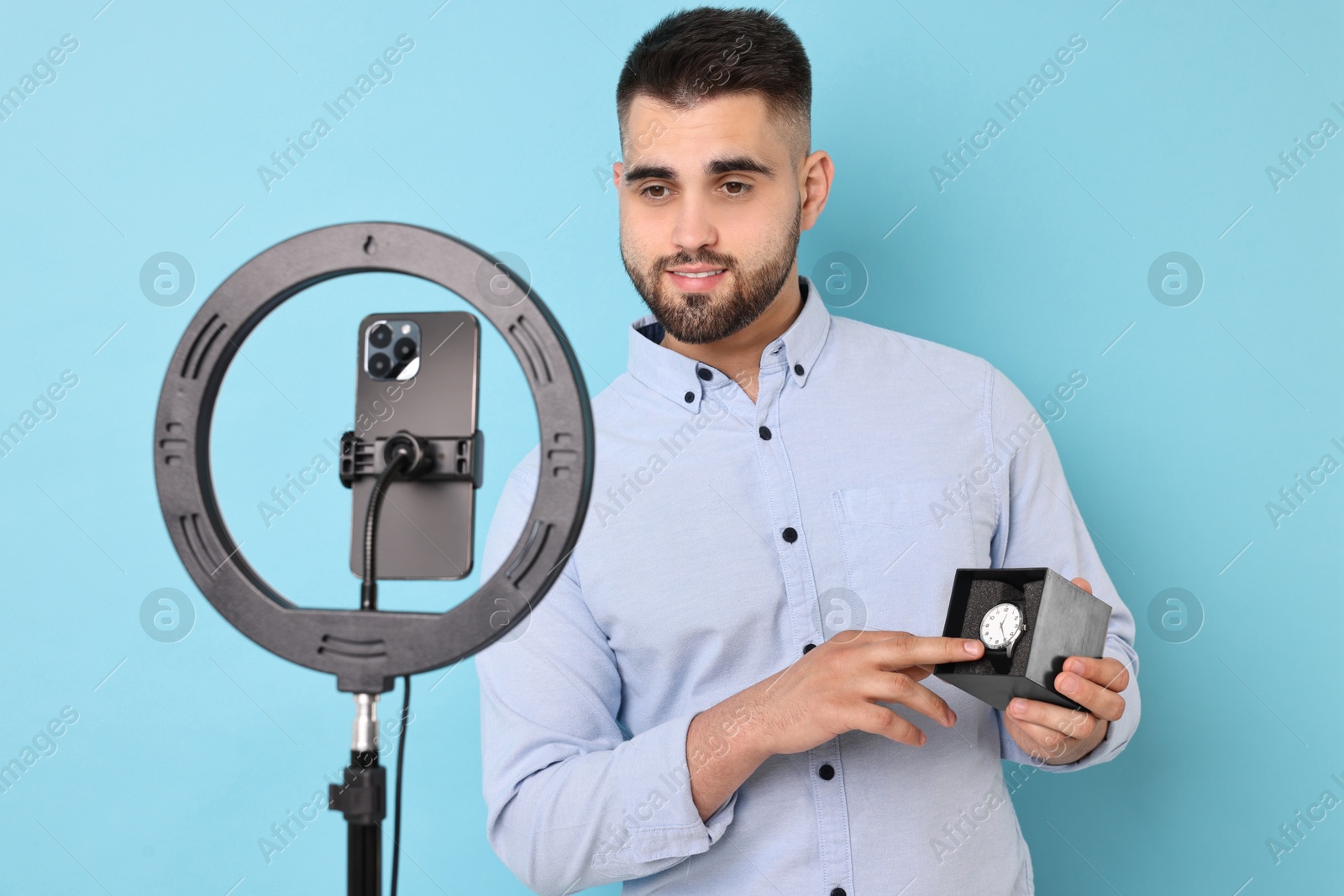 Photo of Fashion blogger reviewing watch and recording video with smartphone and ring lamp on light blue background