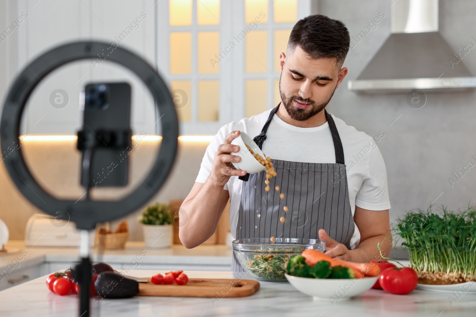 Photo of Food blogger cooking while recording video with smartphone and ring lamp in kitchen